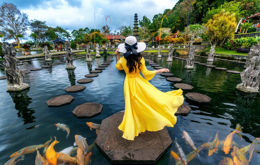 Woman standing in pond with colorful fish at Tirta Gangga Water Palace in Bali, Indonesia.